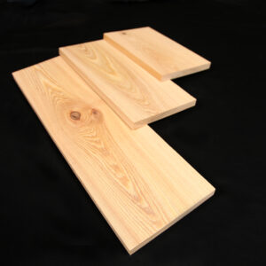 Cypress 1x12. Three light-colored wooden planks with visible grain and a knot arranged in a staggered, overlapping pattern on a black background