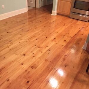Glossy light-pine hardwood floor with visible knots filling a kitchen area beside a stainless-steel stove and light blue wall.