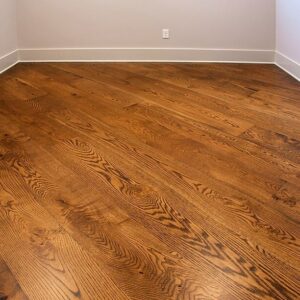 Empty room with warm brown oak hardwood floor planks, white baseboards, and a wall outlet.