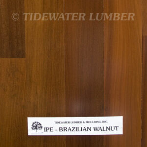 Ipe Flooring Close-up of warm reddish-brown Ipe (Brazilian walnut) wood flooring planks with a white label at the bottom reading “Tidewater Lumber & Moulding, Inc. IPE - BRAZILIAN WALNUT” and a faint “TIDEWATER LUMBER” watermark across the top.