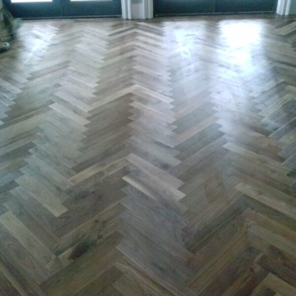 Herringbone-patterned hardwood floor filling a bright room with tall dark-framed glass doors along the far wall letting in diffuse daylight.