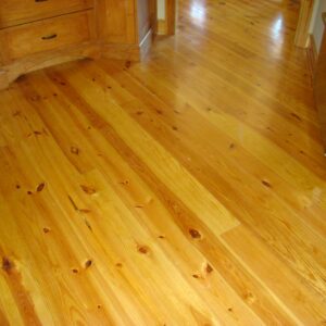 Honey-colored hardwood floor with visible knots and grain in a kitchen between wooden cabinets and a stainless appliance