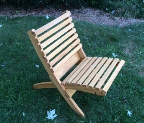 Light-colored wooden slatted outdoor chair with a slightly reclined back and angled legs sitting on green grass.