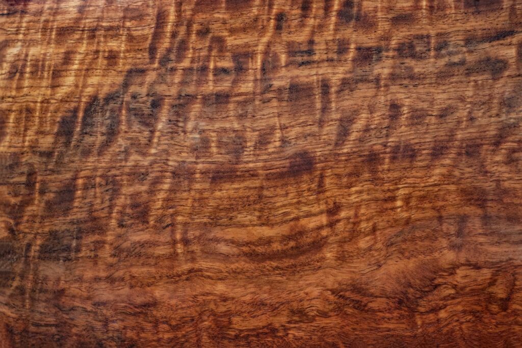 Polished reddish-brown wood surface with rich, wavy grain patterns and fine textured figure.